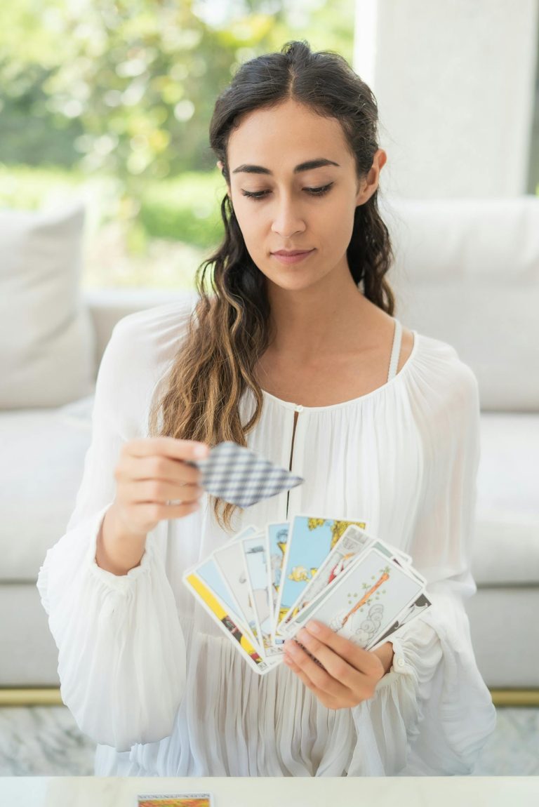 Female in white dress reading tarot cards indoors; a serene moment captured.